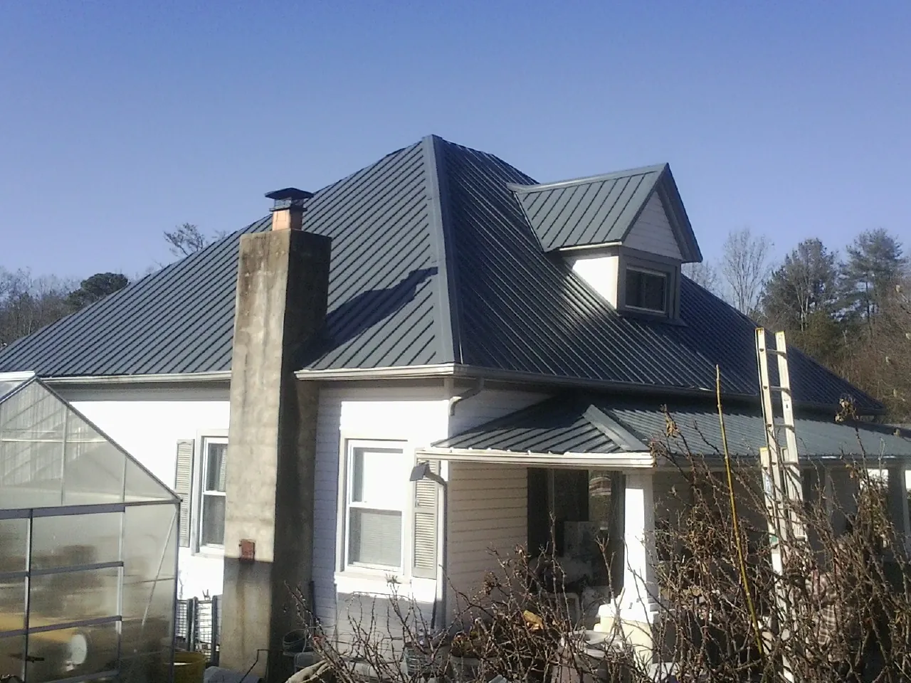 Dark blue standing seam metal roof on a white farmhouse with dormer in Glenelg