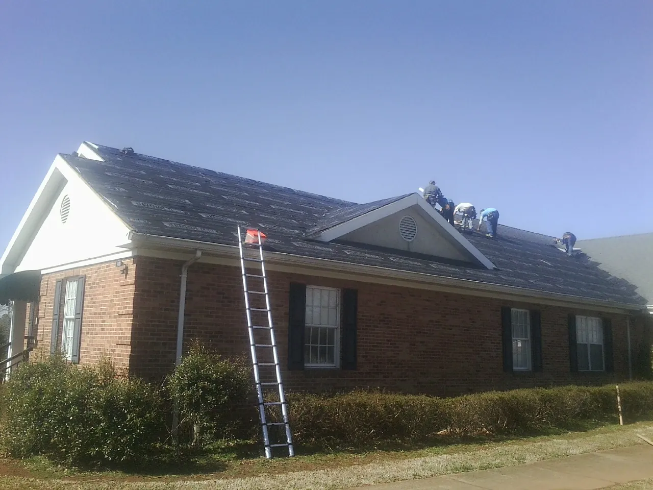 Crew tearing shingles off a brick ranch roof with a ladder set — Metal Roof Repair work by our crew in Glenelg
