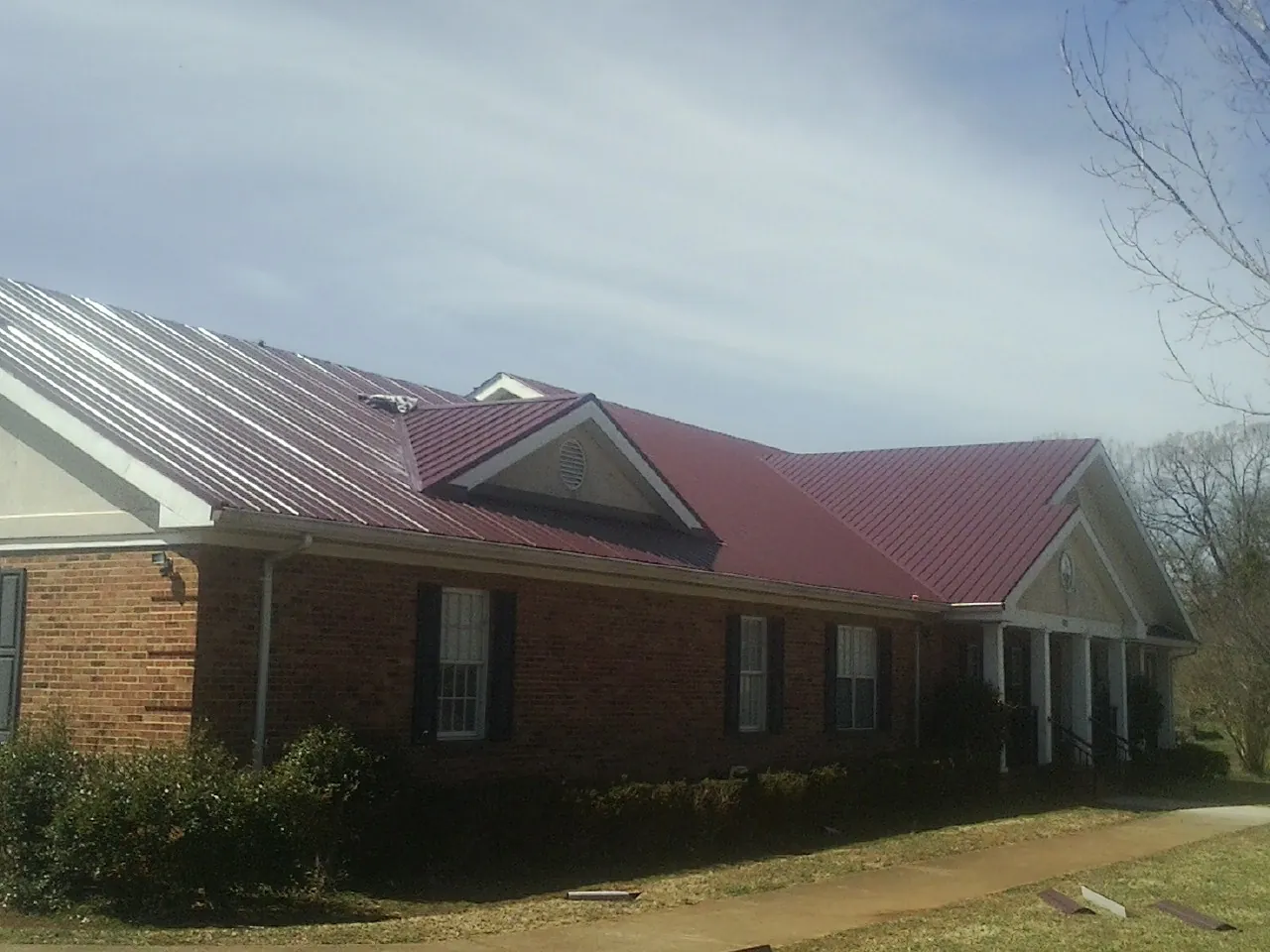 Red metal roof with gabled entries on a long brick building, from a Hail Damage Roof Repair job in Glenelg