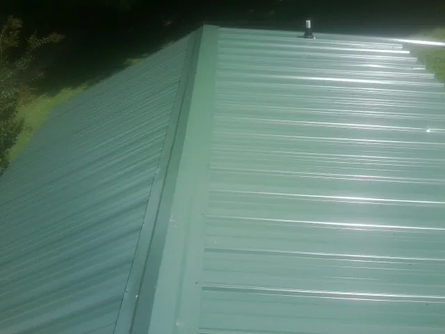 New green metal panels meeting at the ridge of a roof — Flat Roof Repair work by our crew in Glenelg