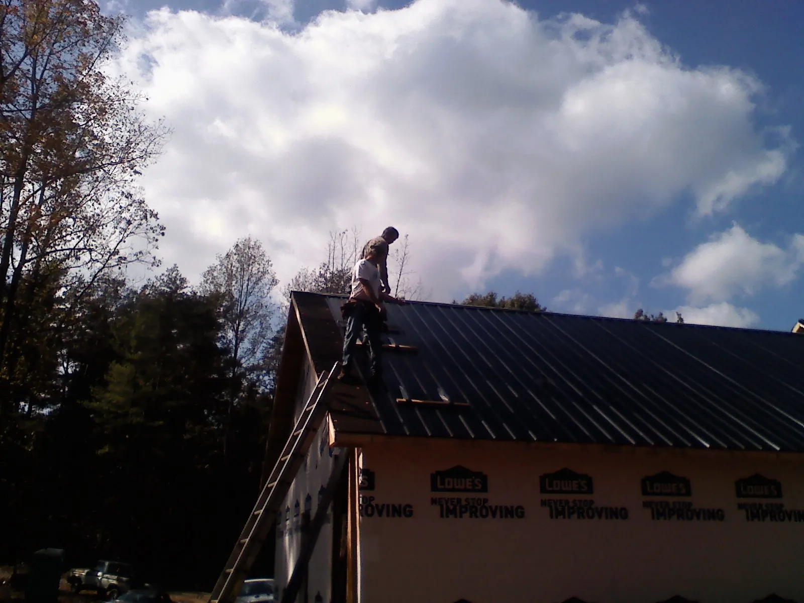 Roofer fastening dark metal panels high against a cloudy sky, from a Roof Inspection job in Glenelg