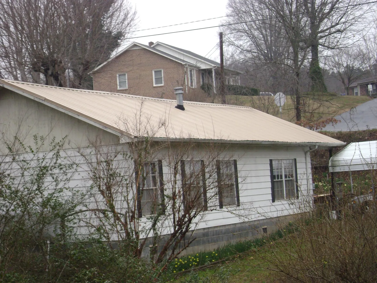 Tan metal roof on a white sided house set into a hillside — Commercial Roofing by Roofing Brothers in Glenelg