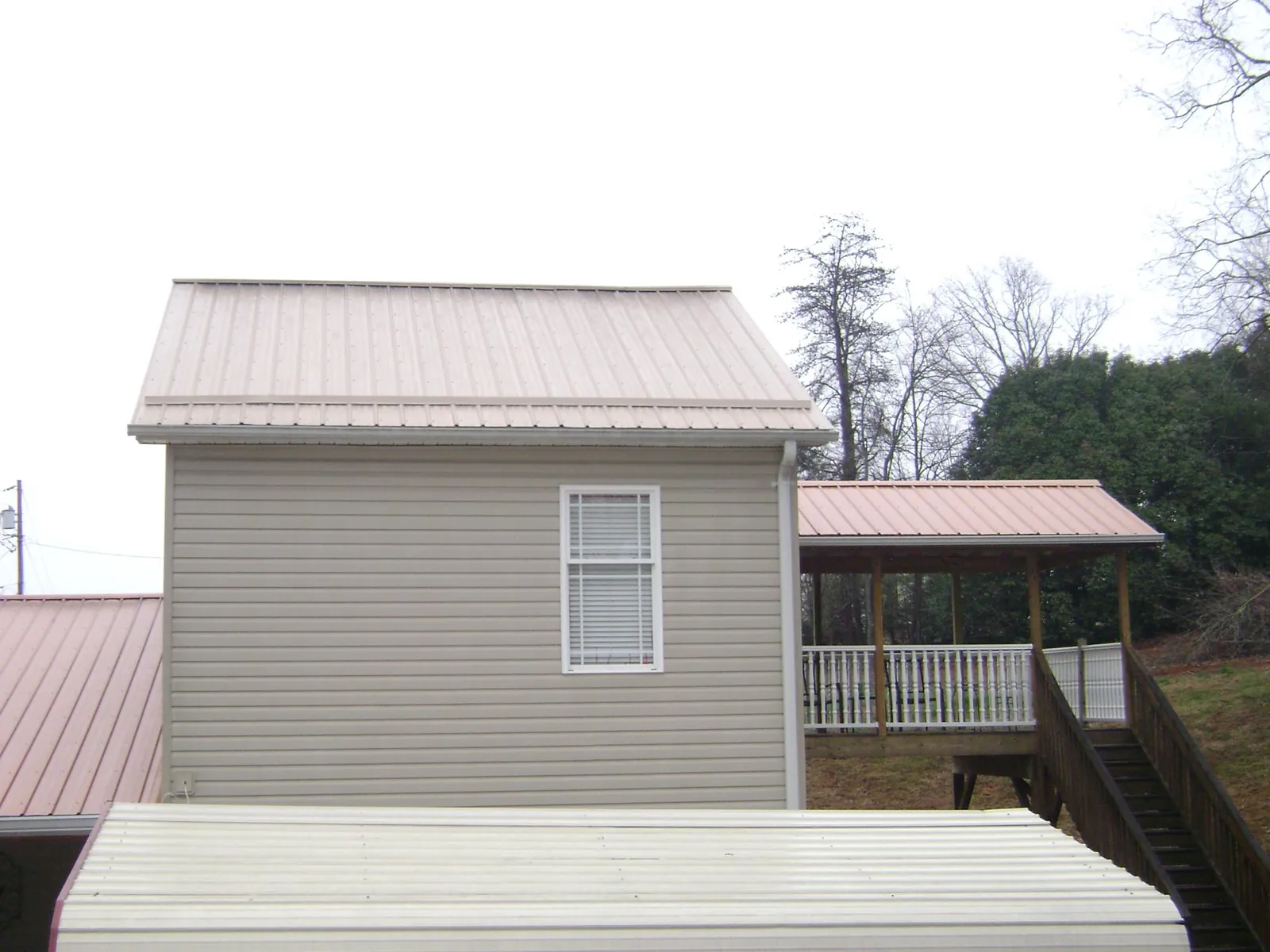 Tan metal roofs on a two story addition and attached porch, from a Roof Replacement job in Glenelg